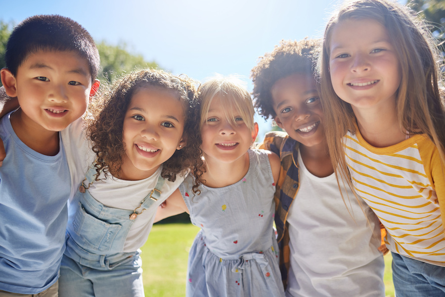 Happy, smile and portrait of kids in a park playing together outdoor in nature with friendship. Happiness, diversity and children friends standing, embracing and bonding in a outside green garden.